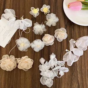 Dettaglio di orecchini floreali in organza bianca con perle e nappe su piano in legno