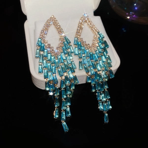 Detailed close-up of golden tassel earrings with blue rectangular gems in a white gift box