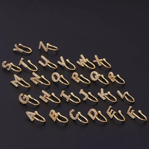 26 gold-plated alphabet nose clips with micro-pave cubic zirconia on a dark background