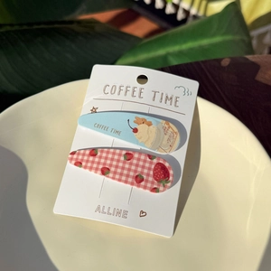 Detail view of strawberry and coffee theme hair clips in a ceramic plate on wooden table