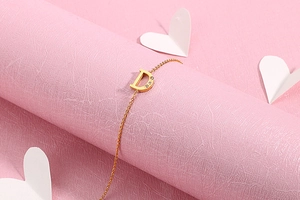 Detail of a gold-tone thin chain bracelet featuring a letter D pendant set with zircons