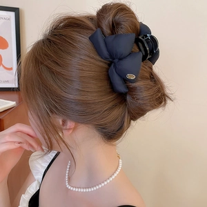 Detail of navy blue quilted bow hair claw clip with golden tag on model hair