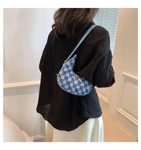 Detail of crescent denim crossbody bag with distressed finish shown on a model