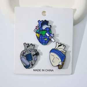 Artistic anatomical heart enamel pins featuring Earth and classic art on white card