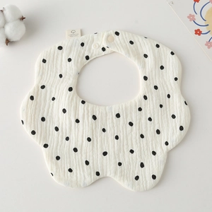 Macro shot of petal-shaped muslin cotton baby bib with black polka dots on beige