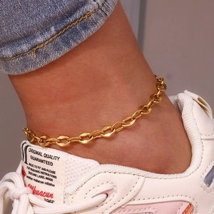 Detail der goldenen Fußkette mit Perle am Knöchel kombiniert mit Jeans und Sneakern