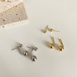 Macro shot of minimalist polished gold and silver spherical stud earrings on stone