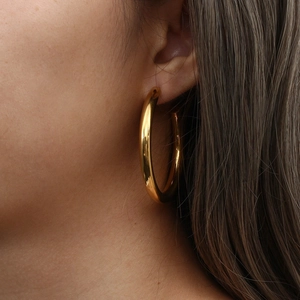 Close-up of chunky gold hoop earring worn by model showing texture and metallic luster