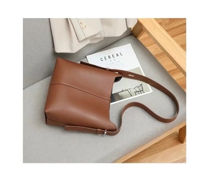 Dettaglio di una borsa a secchiello in pelle marrone con tracolla su un divano grigio