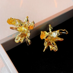 Macro detail of golden petal earrings showing irregular pleated texture and metallic luster