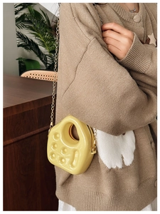Detail of yellow jelly crossbody bag with gold chain strap worn by a model in soft lighting
