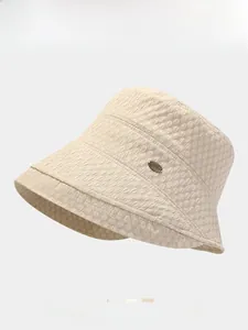 Detail of beige textured bucket hat with an oval metal logo plaque on a clean background