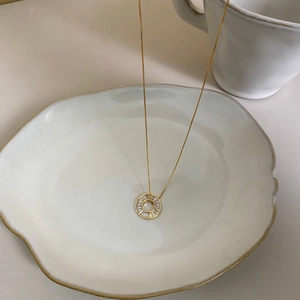 Elegant gold bow necklace with a sparkling round pavé crystal pendant on ceramic tray