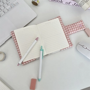 Pink plaid fabric notebook cover with button closure and lined pages on office desk