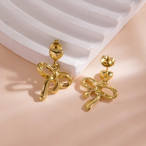 Detailed macro view of 14K gold-plated heart and bowknot drop earrings on textured stand