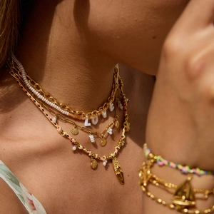 Close-up of gold LOVE pendant necklace with layered pearls and woven summer beach charms