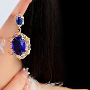 Detailed close-up of a model wearing luxury oval blue zircon earrings in gold finish