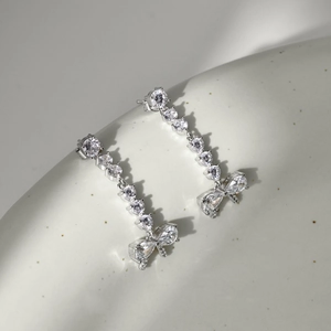 Macro detail of silver drop earrings featuring cubic zirconia and bowknot pendants