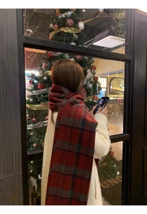 Detail of red and green plaid thick scarf worn by woman near a cozy Christmas tree