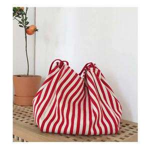 Detail of red and white striped canvas bag with drawstring on wooden bench with plant