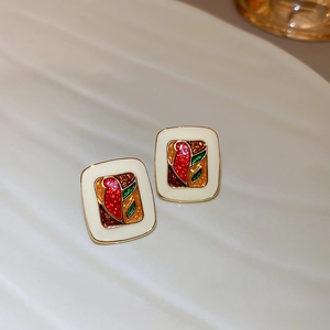 Close-up of vintage square enamel earrings with colorful patterns on a white plate