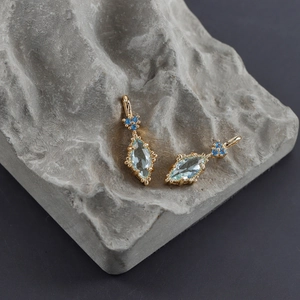 Macro shot of 18k gold earrings with marquise blue stone on a grey stone base