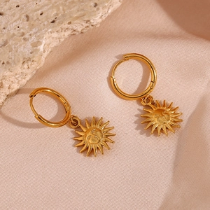 Macro detail of golden sun pendant earrings on elegant pink silk and stone texture