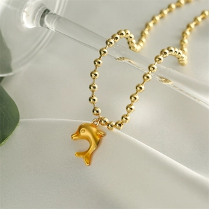 Close-up of a gold-plated dolphin pendant on a beaded chain over white silk fabric