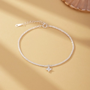 Detail of S925 silver bracelet featuring clover pendant and moonstone charm on warm background