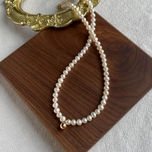 Detailed view of Baroque freshwater pearl necklace with gold ball pendant on wood