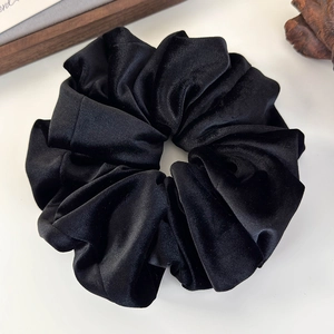 Macro detail of soft black velvet texture and dense pleats on large scrunchie