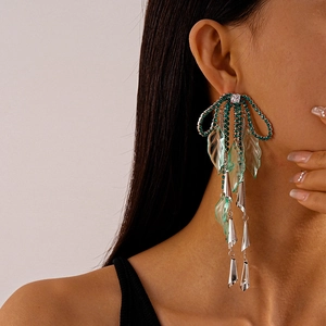 Macro detail of long tassel earrings with green rhinestones and resin leaves for women