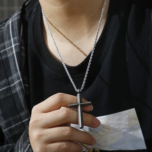 Close-up of silver cross pendant with twisted chain worn over a casual black shirt