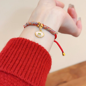 Détail d'un bracelet en corde rouge tissé main avec pendentif en émail doré et nœuds
