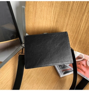 Detail of black leather texture on square crossbody bag with silver buckle and wide strap