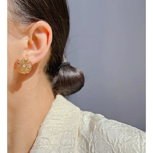 Close-up of model wearing gold sunburst stud earrings with polished metallic finish