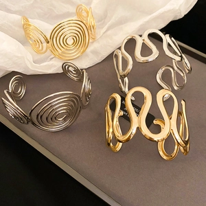Close-up of geometric spiral and S-shaped wavy gold and silver metal open bracelets