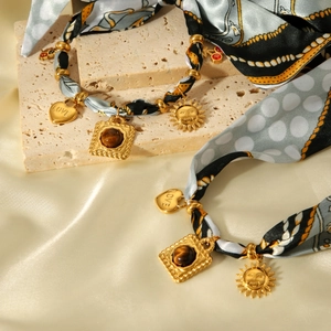 Detail of silk scarf bracelet with gold heart love pendant and vintage sun charm