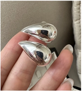 Silver hollow teardrop earrings held by hand showing size scale and glossy finish
