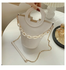 Detail of cream white bucket bag featuring round cutout handle and thick chain strap