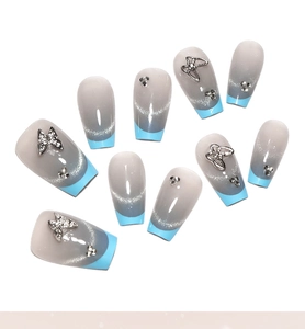 Détail des faux ongles œil de chat bleu avec papillons 3D et décorations en strass
