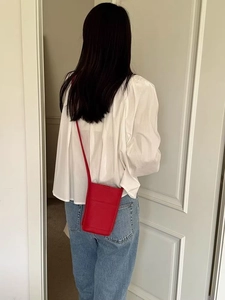 Red leather mini crossbody bag with slim strap shown on shoulder against a white door