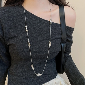 Detailed view of long silver necklace with irregular fluid pendants on a grey sweater