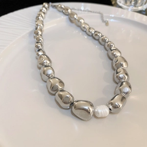 Detailed view of silver irregular beads and white pearl pendant on a white ceramic plate