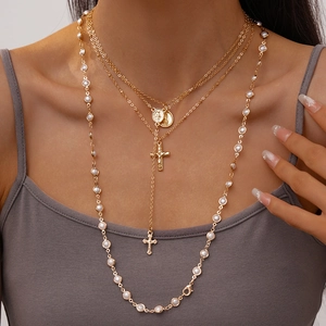 Detail of layered gold necklace featuring pearl strands, cross charms and oval icons