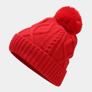 Detail of red cable-knit beanie with fluffy pom-pom and thick warm texture for winter