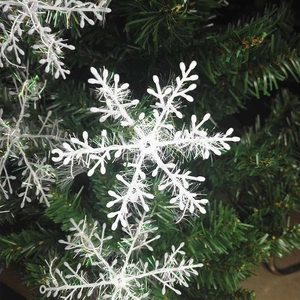 Detailed view of a white plastic snowflake ornament hanging on green Christmas tree branches