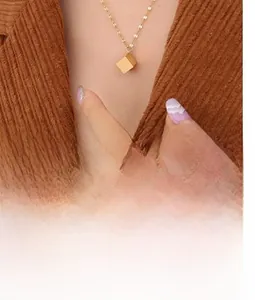 Minimalist gold cube pendant necklace shown on model with corduroy background