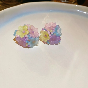 Macro detail of colorful resin flower beaded earrings in a white ceramic dish