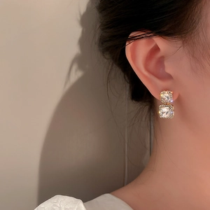 Detail view of gold square drop earrings with sparkling crystals worn by a model